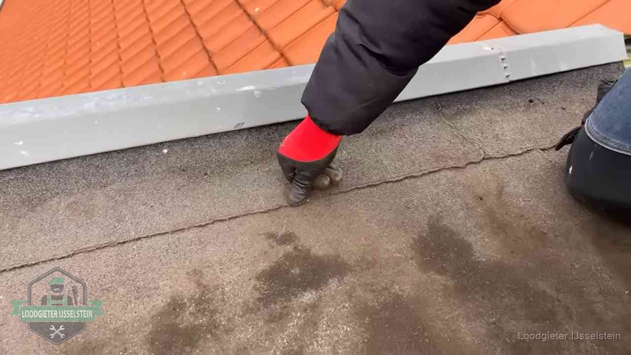 Vakman wijst een naad met vochtplekken aan op een bitumen plat dak in IJsselstein