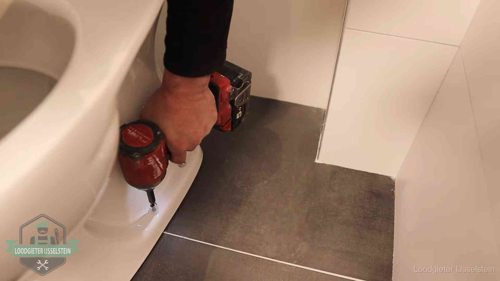 Loodgieter zet de voet van een wc-pot vast op de tegelvloer in IJsselstein